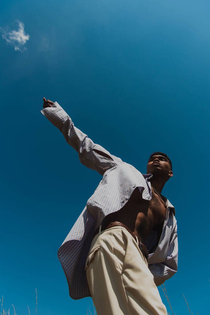 low angle view of trendy african american man with outstretched hand against clear sky - Fotó, kép