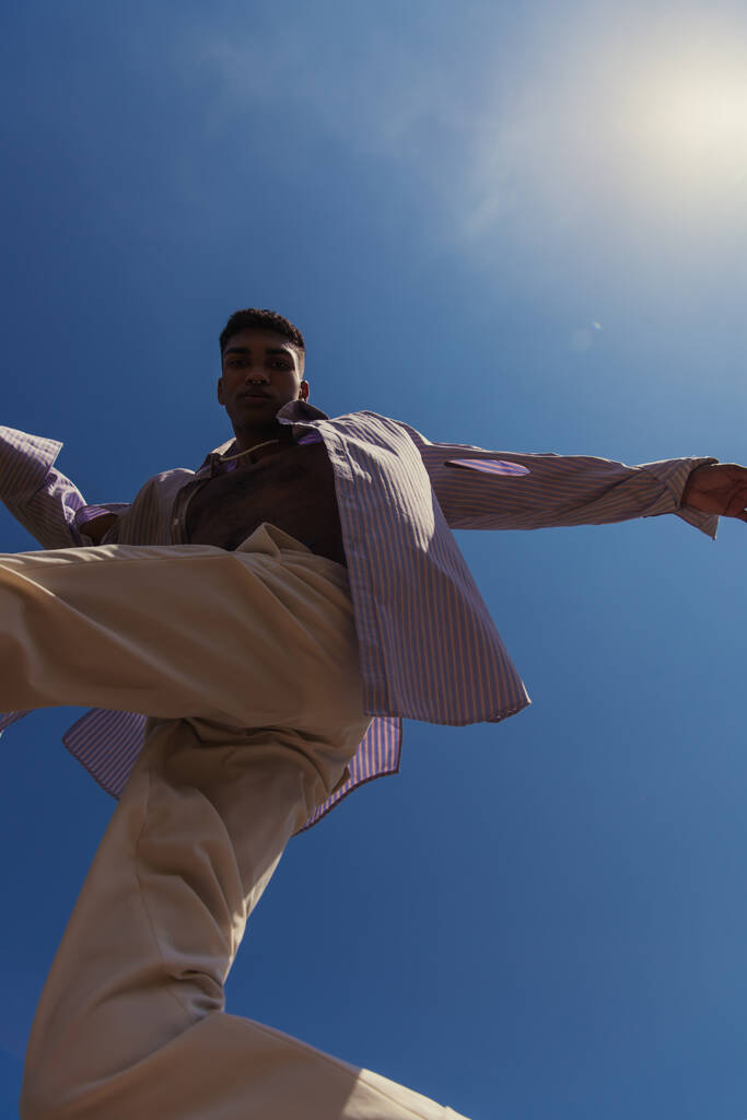 bottom view of african american man in trendy clothes under blue and clear sky - Foto, Imagem