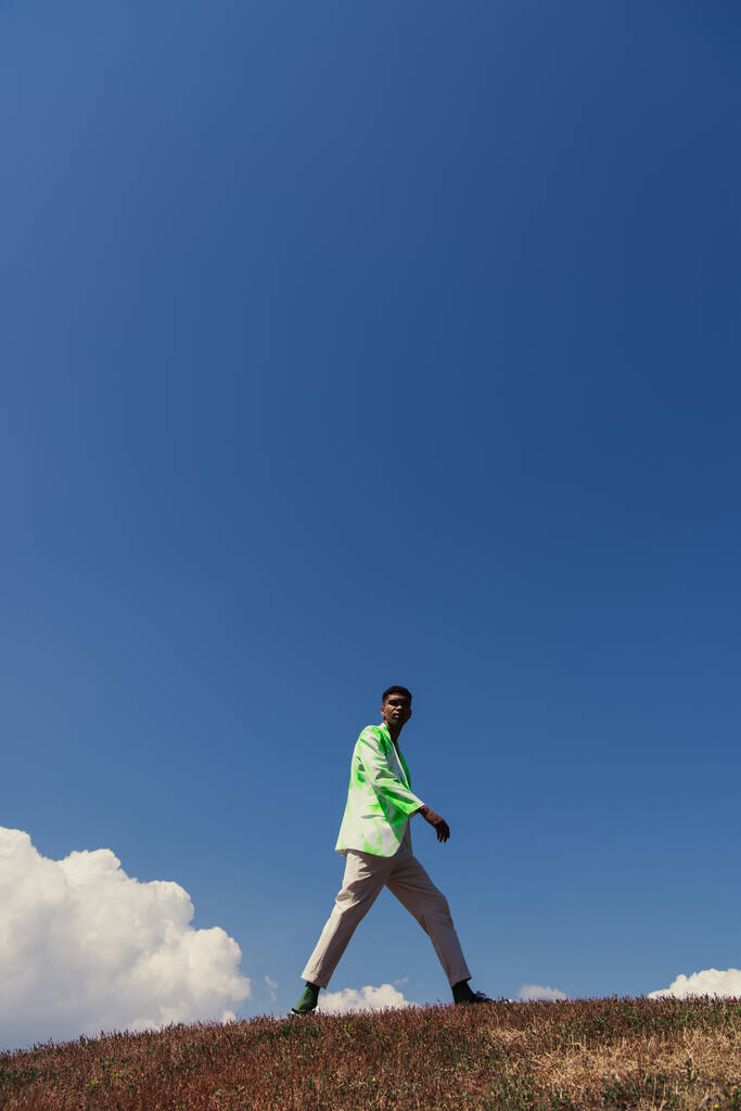 stílusos afro-amerikai férfi nyári ruhában áll zöld mező alatt kék ég - Fotó, kép