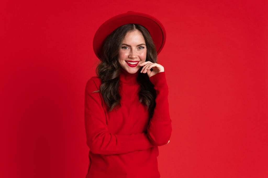Weiße Frau mit Hut, die vor rotem Hintergrund isoliert in die Kamera blickt und lächelt - Foto, Bild