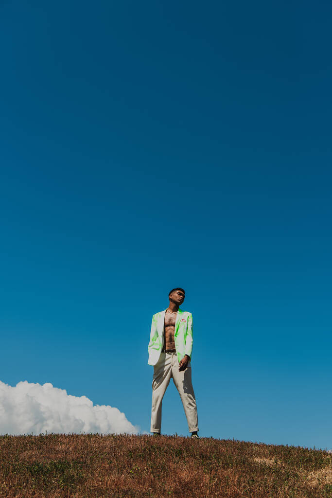 módní africký Američan muž v letním oblečení stojící na poli pod modrou oblohou - Fotografie, Obrázek