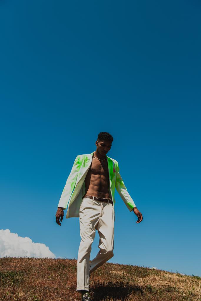 african american man in white and green blazer walking in field on summer day - Φωτογραφία, εικόνα