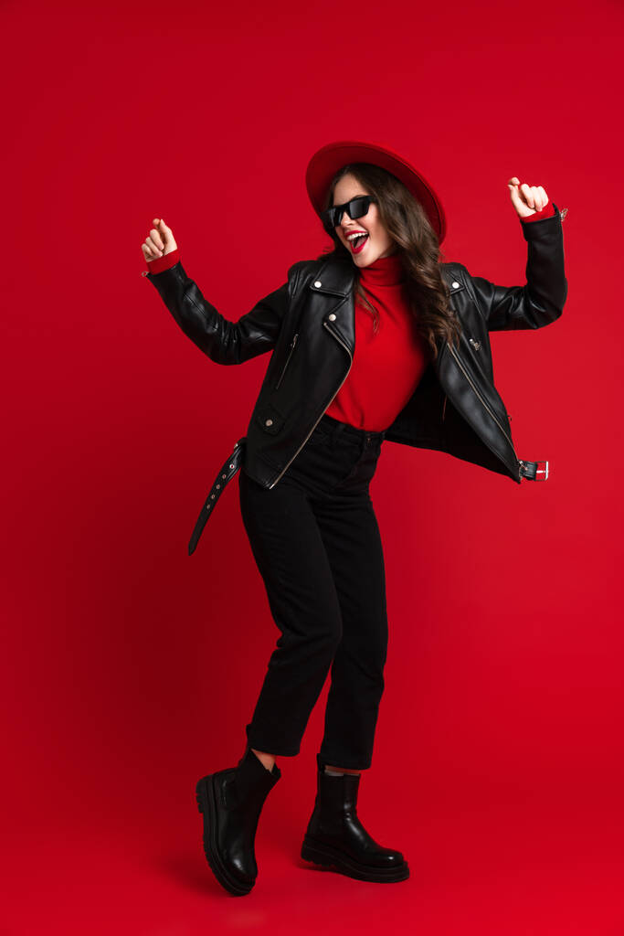 White woman in leather jacket laughing while dancing on camera isolated over red background - Foto, Imagem