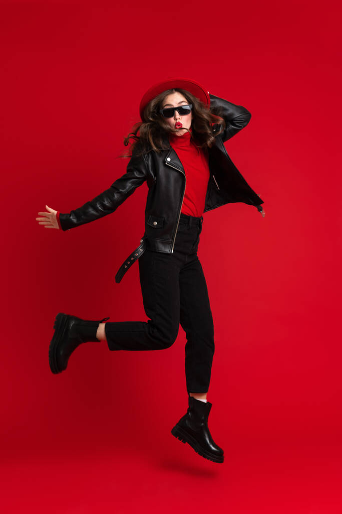 White woman in leather jacket laughing while dancing on camera isolated over red background - Photo, Image