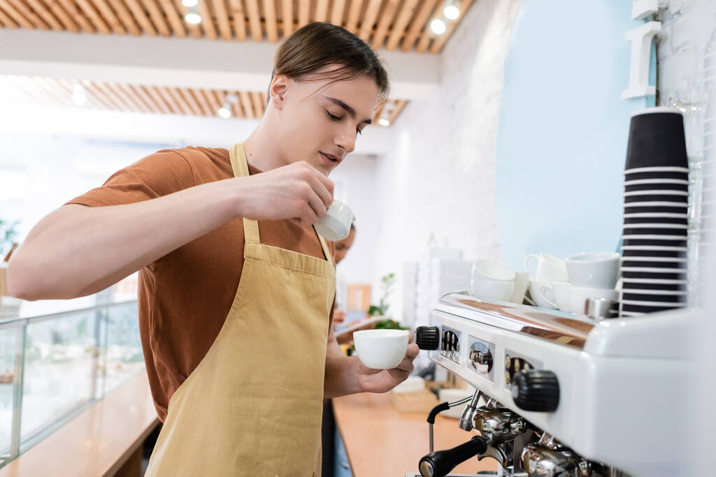 Young barista making coffee near machine in confectionery  - Фото, изображение