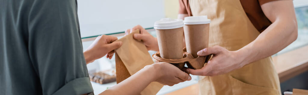 Cropped view of african american client taking coffee to go and paper bag from seller in sweet shop, banner  - Fotoğraf, Görsel