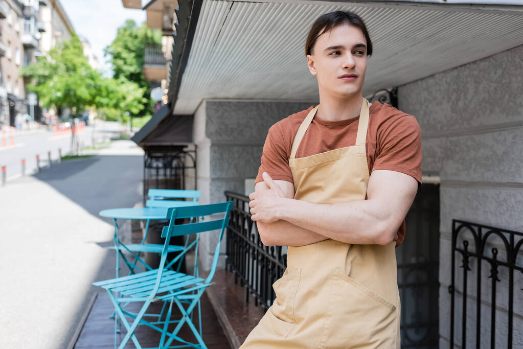 Young salesman in apron looking away on terrace of sweet shop  - Zdjęcie, obraz