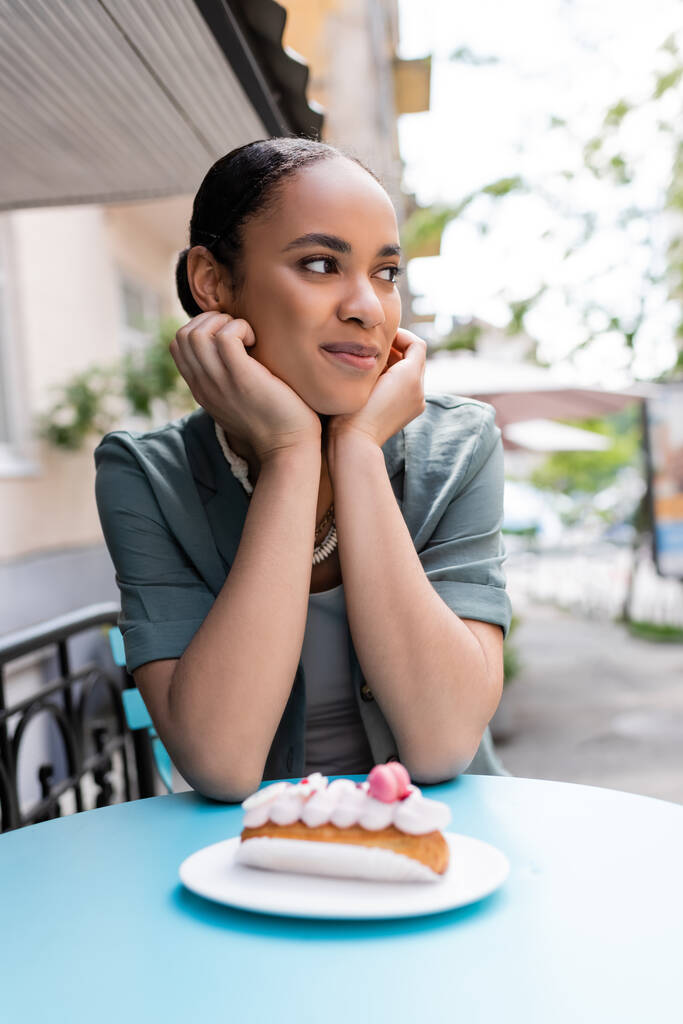 jong Afrikaans amerikaans cliënt kijken weg in de buurt wazig dessert op terras van zoetwaren  - Foto, afbeelding