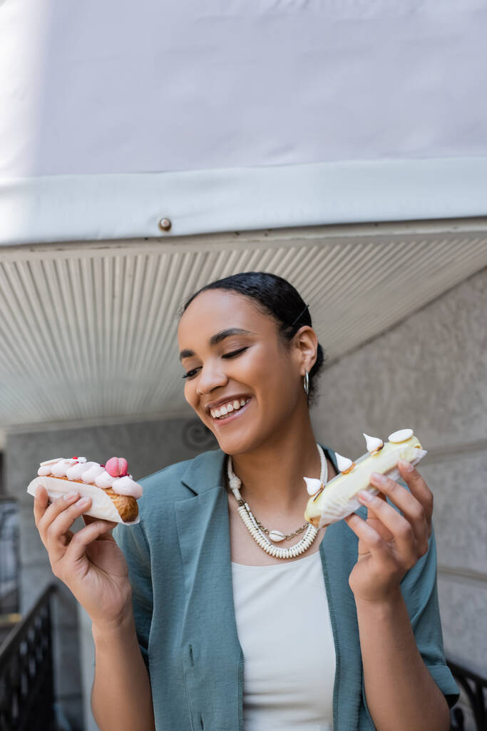 Pretty african american woman holding eclairs on terrace of cafe  - Foto, Imagem