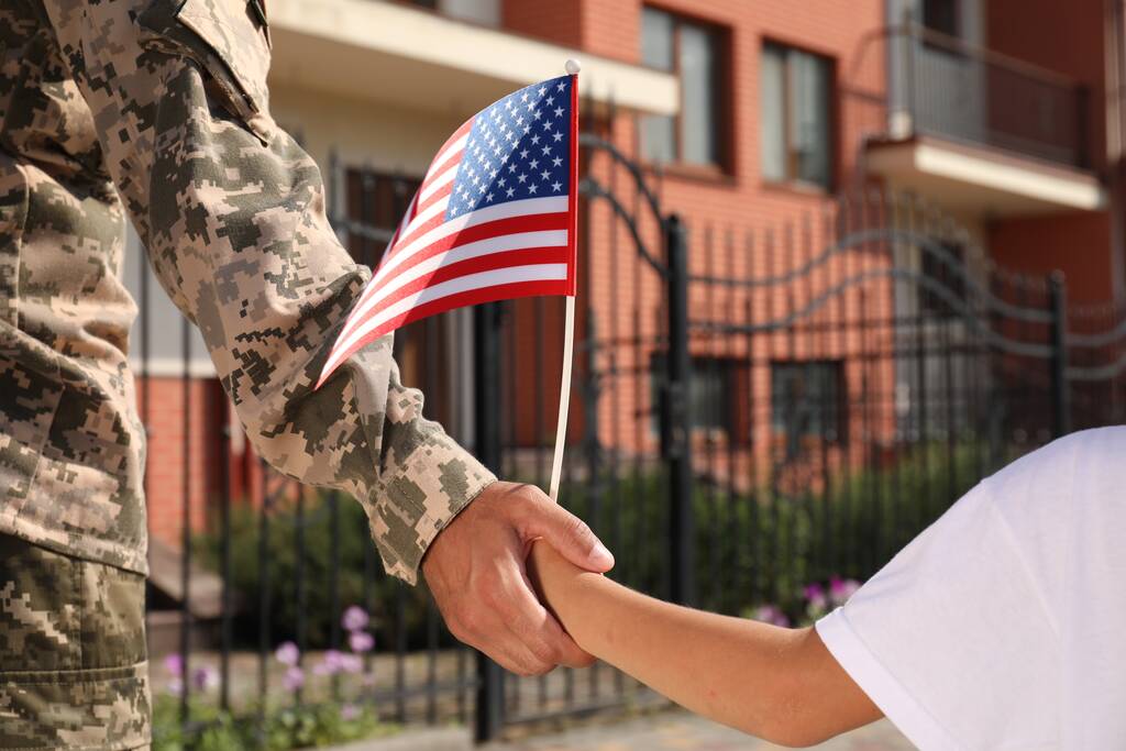 Soldado y su hijito con bandera americana tomados de la mano al aire libre, de cerca. Día de los Veteranos en Estados Unidos - Foto, Imagen