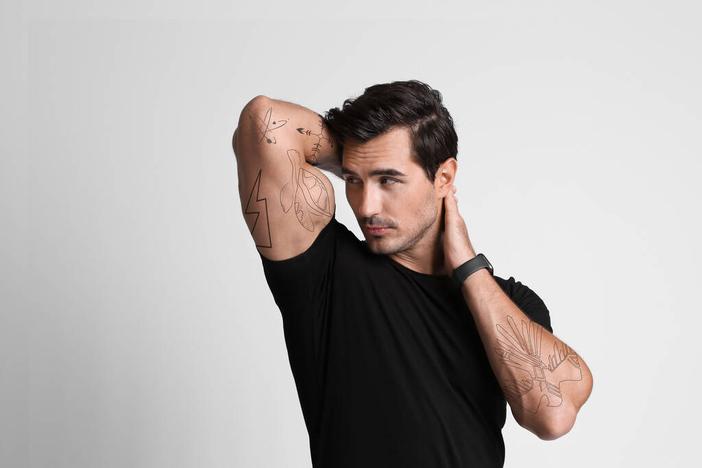 Handsome man with beautiful tattoo sketches on light grey background - Zdjęcie, obraz
