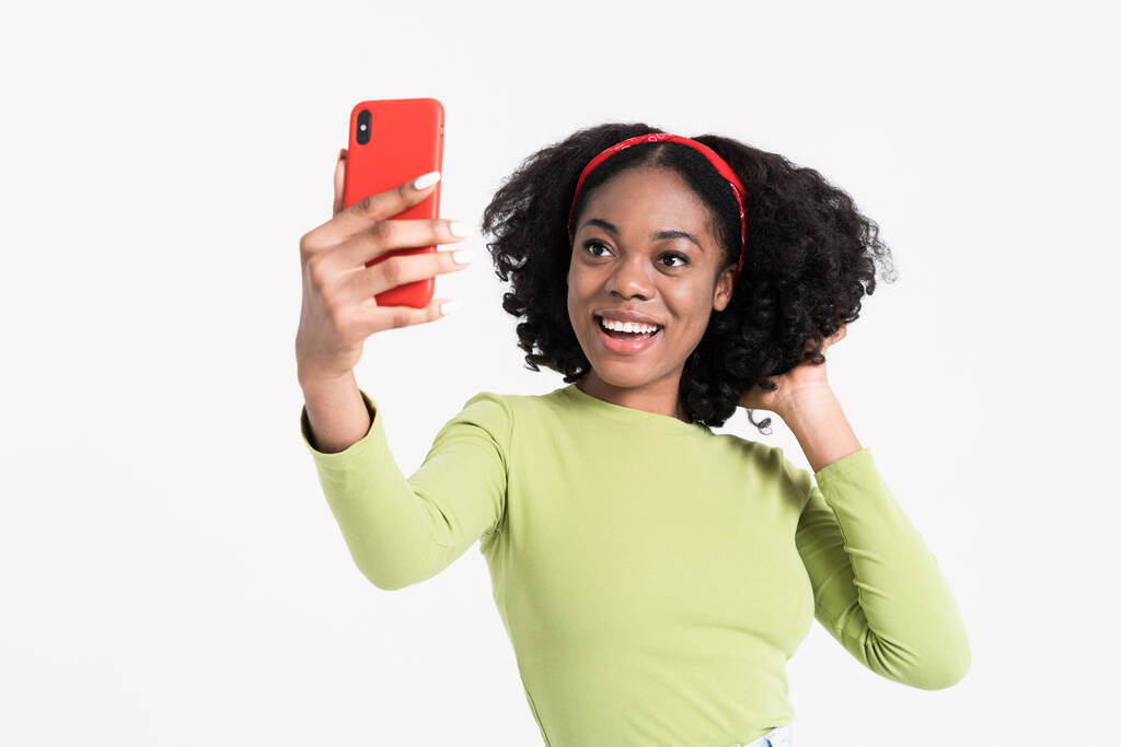 Young black woman smiling while taking selfie photo on cellphone isolated over white background - Photo, image
