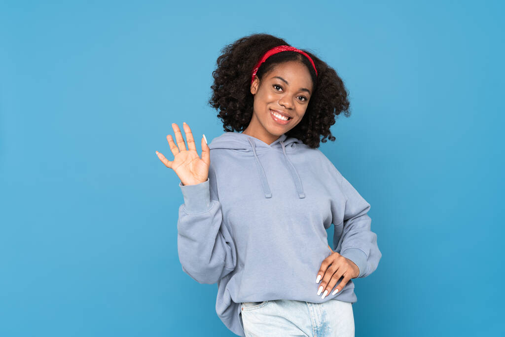 Young black woman wearing headband smiling and gesturing at camera isolated over blue background - Foto, Imagem