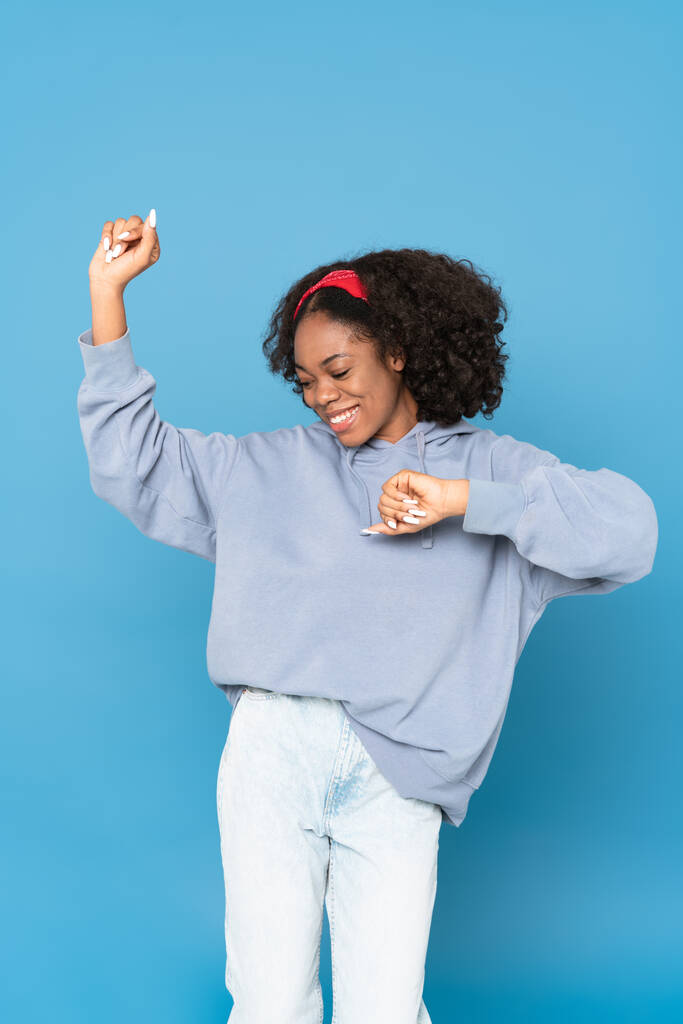 Young black woman wearing headband smiling while dancing isolated over blue background - Foto, afbeelding