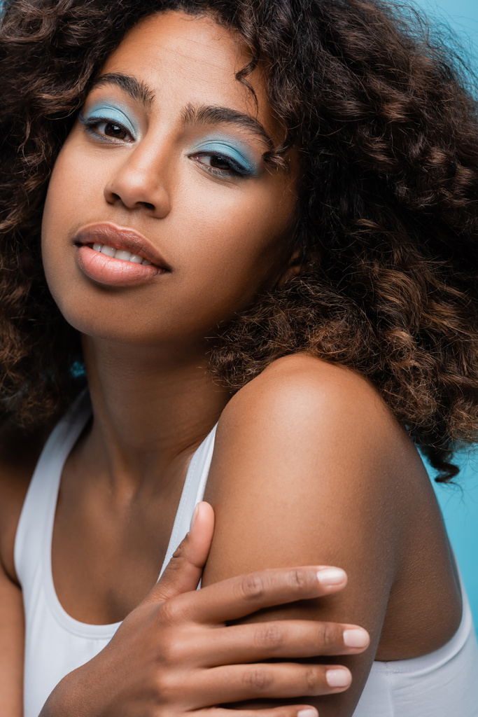 portrait of african american woman with wavy hair and makeup on perfect face isolated on blue - Foto, immagini