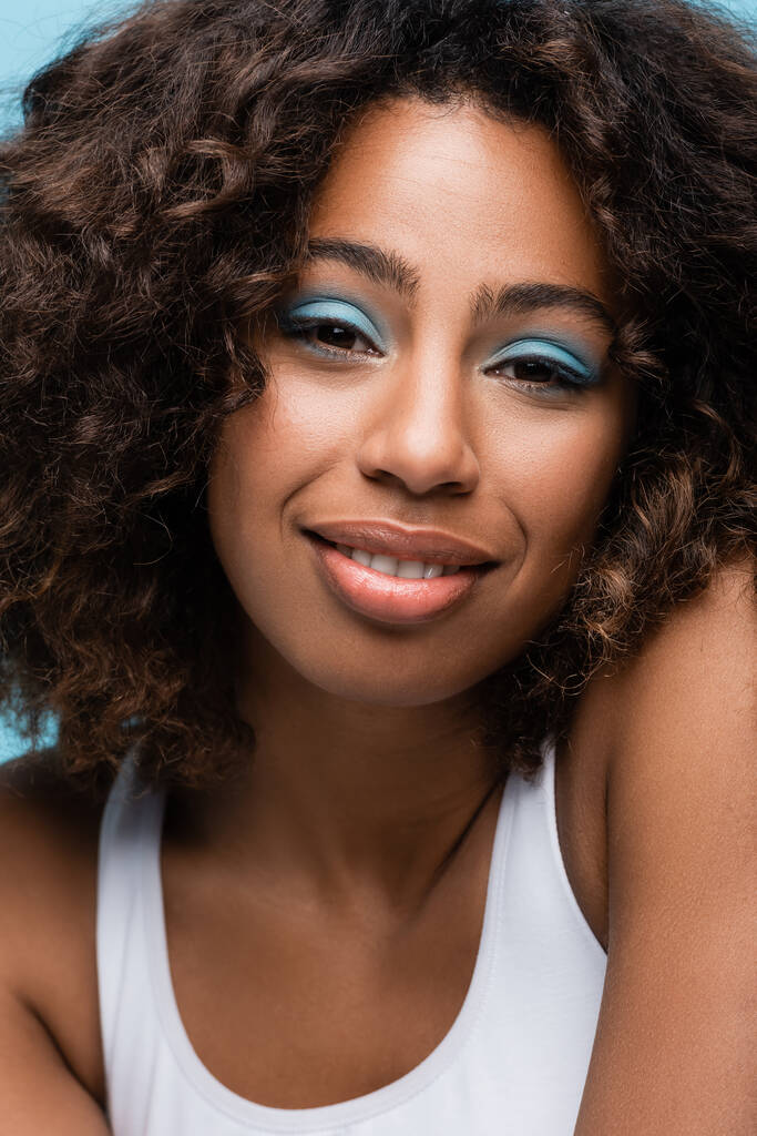 Dalgalı saçlı ve makyajlı Afro-Amerikan kadın portresi mavi üzerine izole edilmiş. - Fotoğraf, Görsel