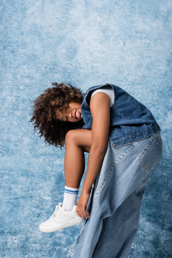 trendy african american woman in ripped jeans smiling at camera on blue background - Φωτογραφία, εικόνα