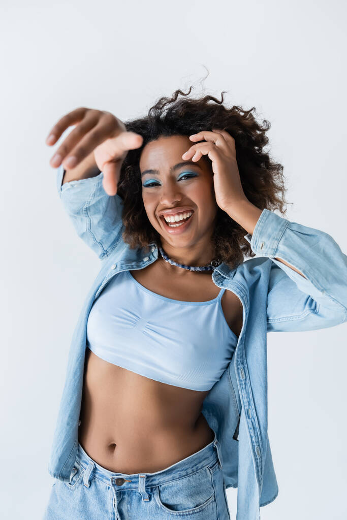 african american woman in white crop top and blue denim shirt pointing with finger at camera isolated on grey - Zdjęcie, obraz