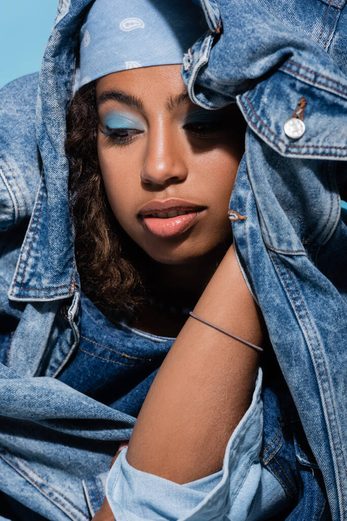 african american woman with makeup posing with denim jacket isolated on blue - Zdjęcie, obraz