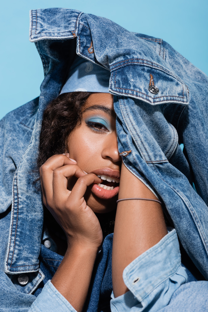 sensual african american woman obscuring face with denim jacket isolated on blue - Φωτογραφία, εικόνα