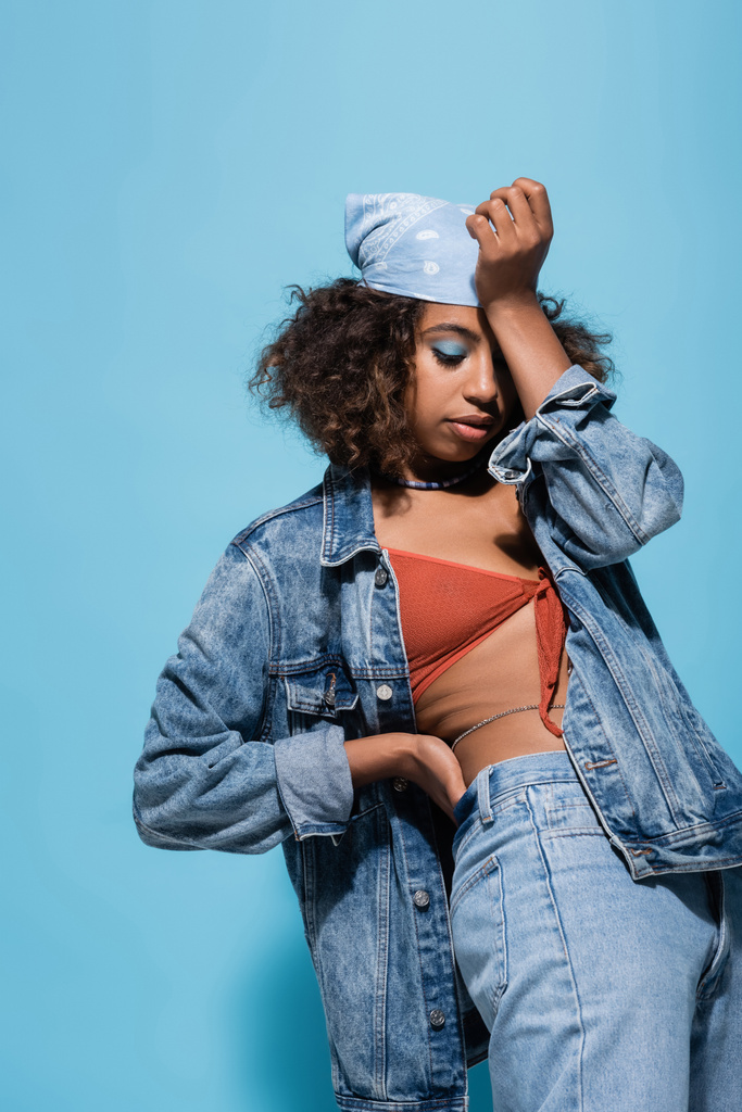 african american woman in swim bra and jacket obscuring face with hand on blue background - Photo, Image