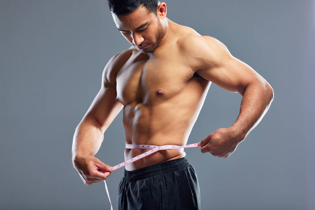 Body goals on fleek. Studio shot of a muscular young man measuring his waist against a grey background - Foto, Imagem