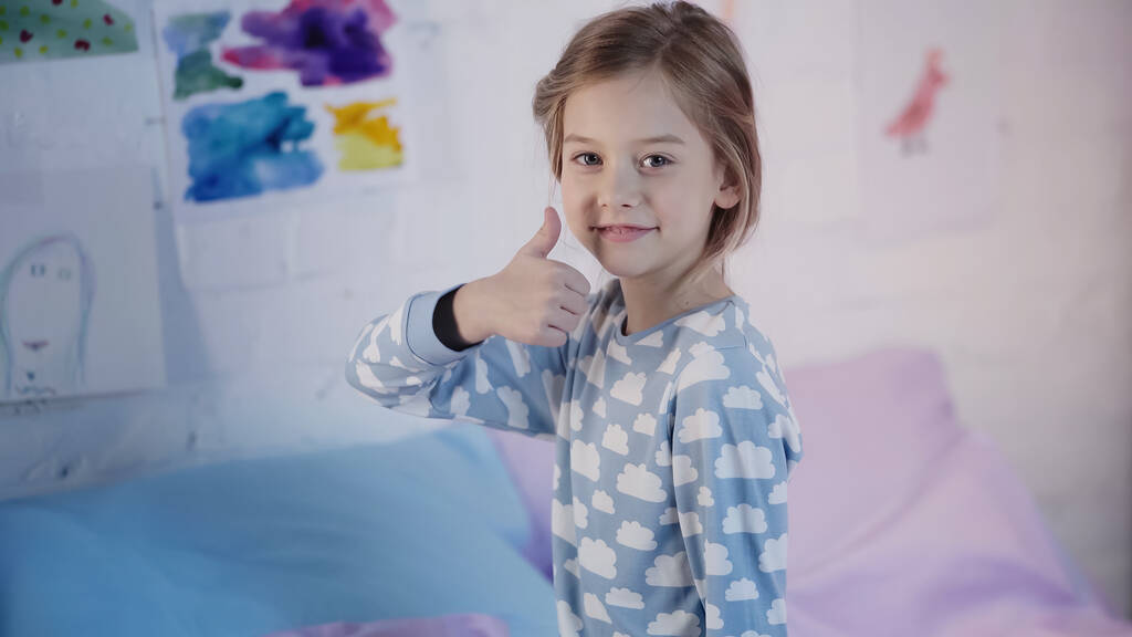 Усміхаючись, дев'ятнадцять дітей у піжамі показують, як жест на ліжку вдома
  - Фото, зображення