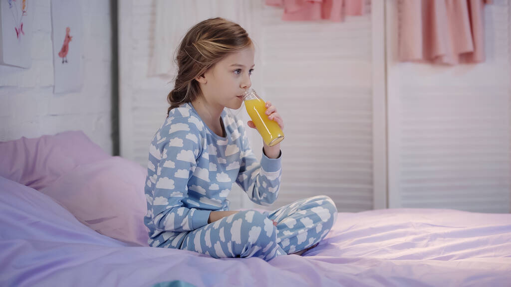 Preteen kid drinking orange juice on bed in evening  - 写真・画像