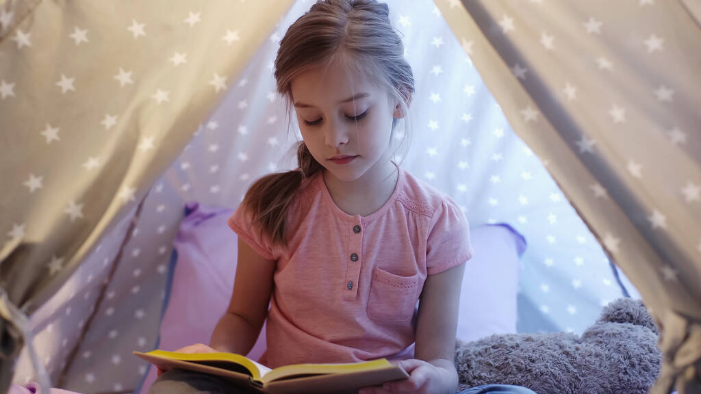Preteen kid reading book in wigwam with lighting at home  - Foto, Imagem