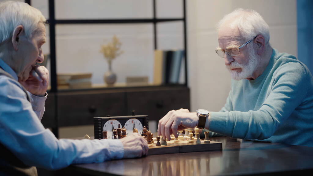 bearded man in eyeglasses playing chess with thoughtful friend at home - Fotografie, Obrázek
