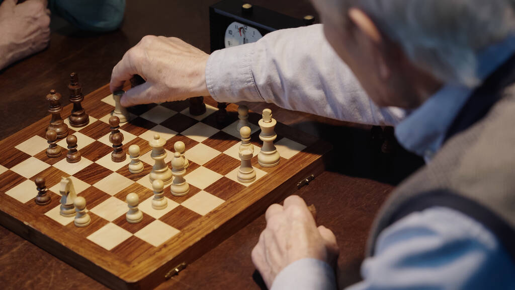 cropped view of blurred senior man moving figure on chessboard while playing with friend - Photo, image