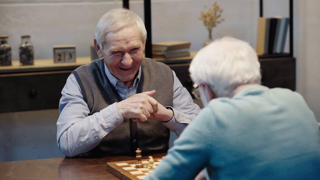 laughing man playing chess with senior friend on blurred foreground - Valokuva, kuva