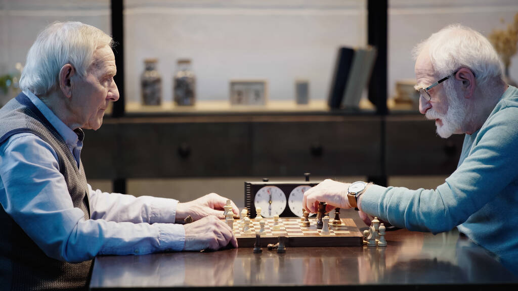 вид збоку на старших сіроволосих чоловіків, які грають у шахи у вітальні
 - Фото, зображення