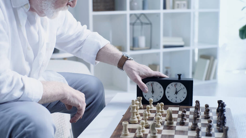 cropped view of senior man using timer near chessboard at home - Fotó, kép