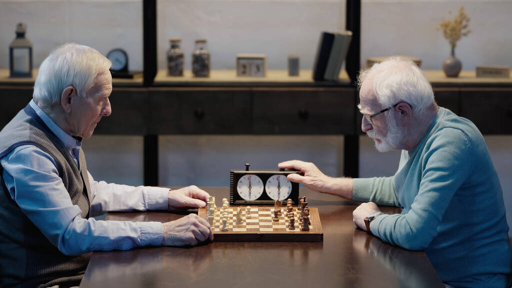 side view of senior man gaming with friend fixing time on chess clock - Photo, image