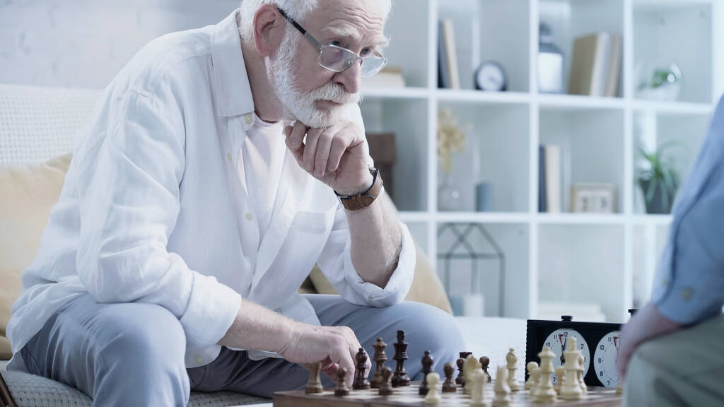 senior bearded man thinking near chessboard and blurred friend - Photo, Image