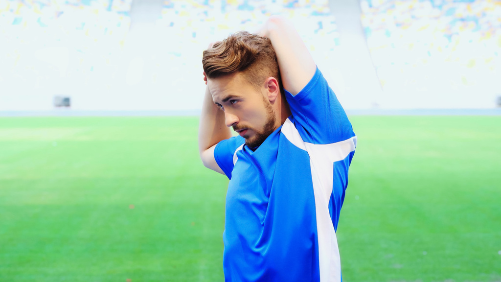 bearded football player in blue t-shirt warming up on green field of stadium - Foto, Bild