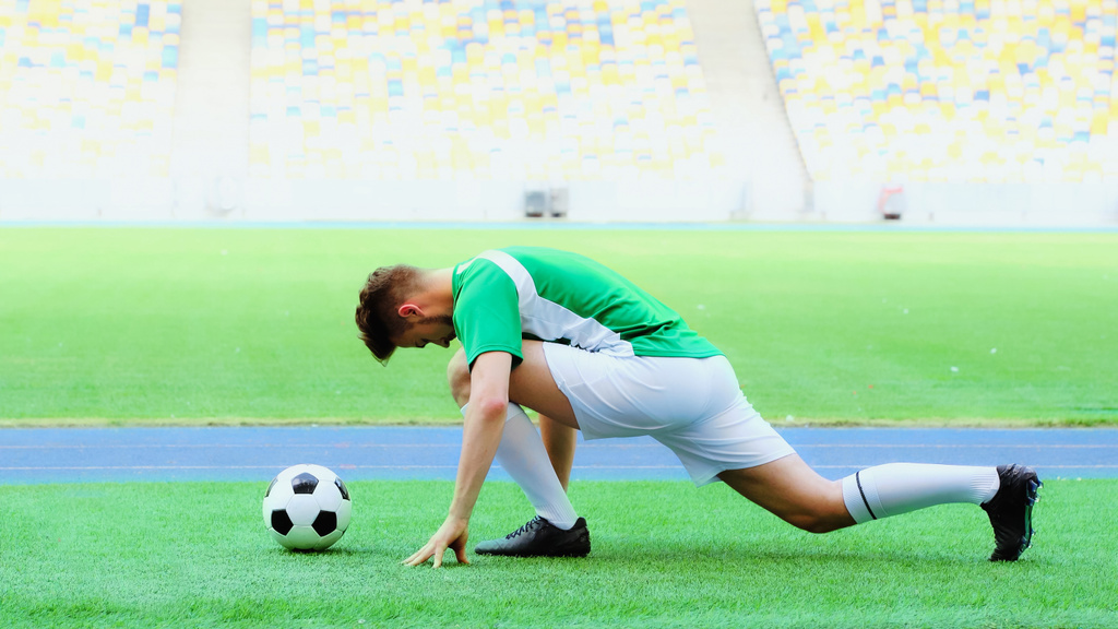 young football player in uniform stretching legs on green grass bear soccer ball  - Foto, Bild