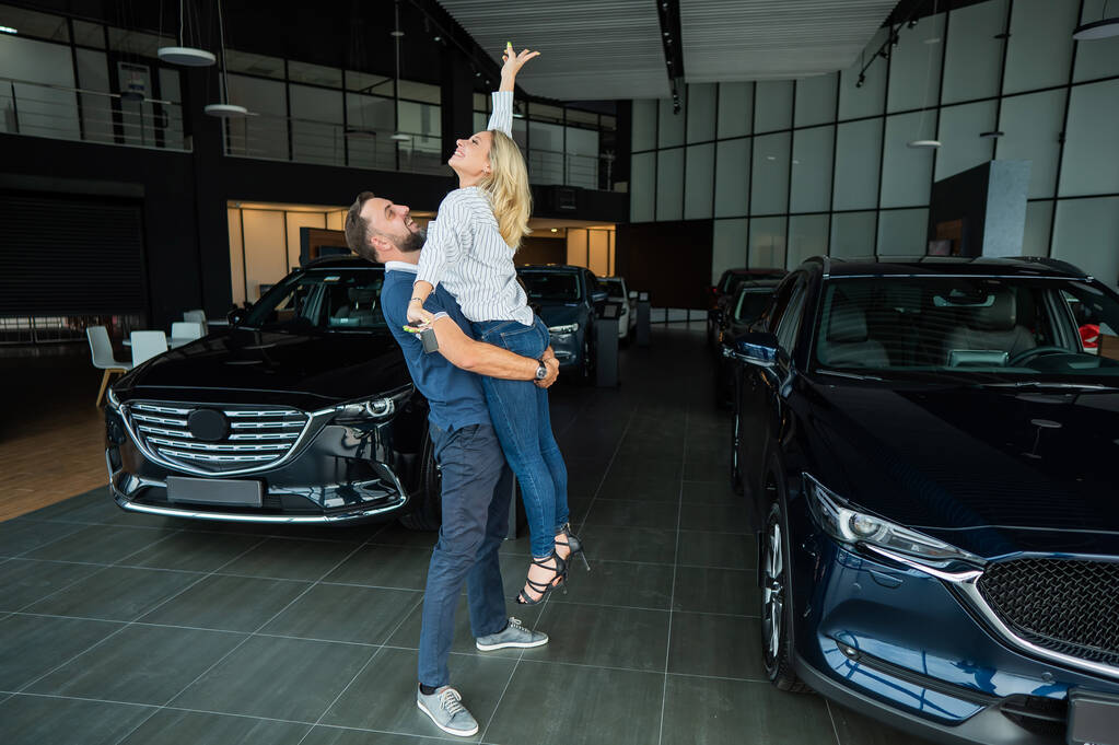 Feliz pareja caucásica abrazando mientras compra un coche nuevo en un concesionario de coches - Foto, imagen