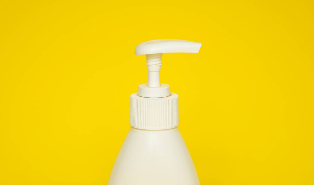 White plastic soap or shampoo dispenser pump bottle isolated on yellow background. Skin care lotion. Bathing essential product. Shampoo bottle. Bath and body lotion. Fine liquid hand wash - Foto, Bild