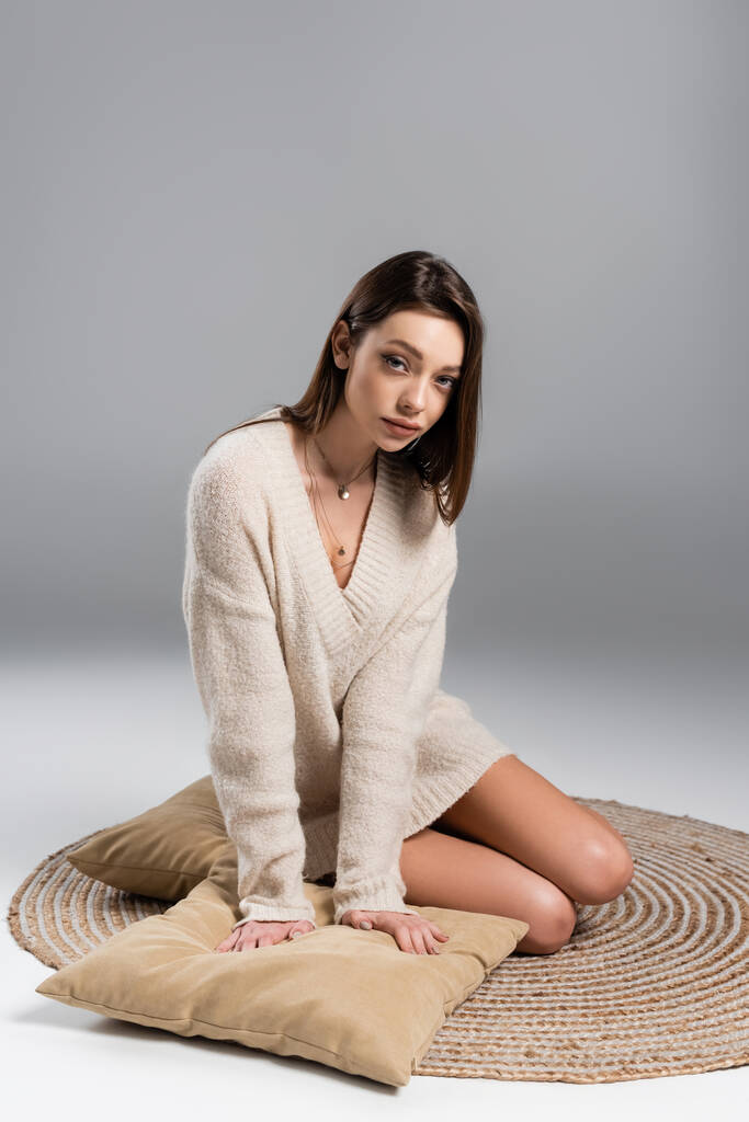 pretty woman with bare legs sitting on rug near pillows on grey background - Fotografie, Obrázek
