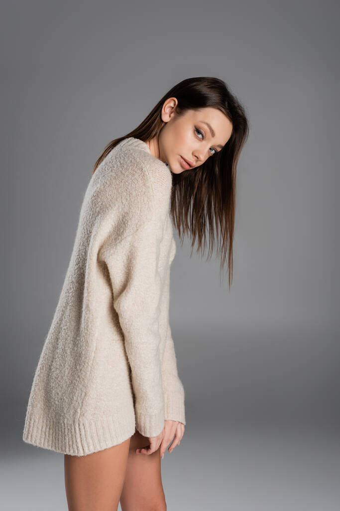 brunette woman in long and soft sweater looking at camera on grey background - Fotó, kép