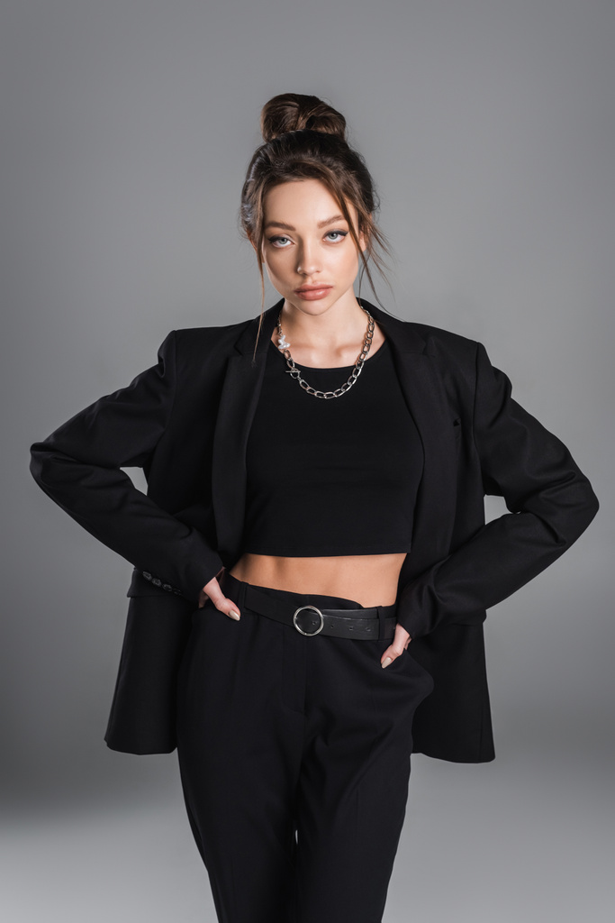 pretty woman in crop top and black suit standing with hands on hips isolated on grey - Foto, immagini