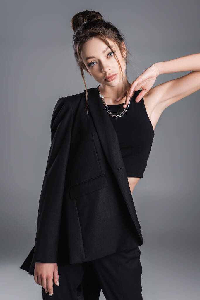 stylish woman in silver necklace posing with black jacket isolated on grey - 写真・画像