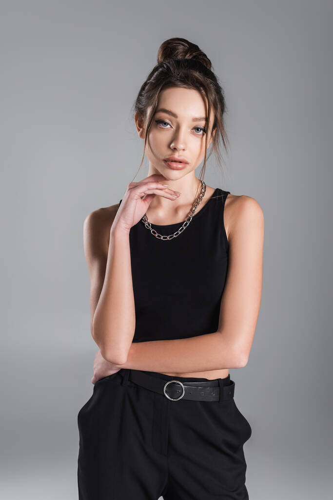 pretty woman in black crop top holding hand near chin while posing isolated on grey - Fotoğraf, Görsel