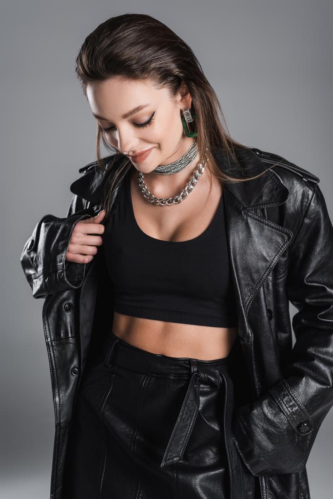 pretty woman in black leather clothes and silver necklaces smiling isolated on grey - 写真・画像