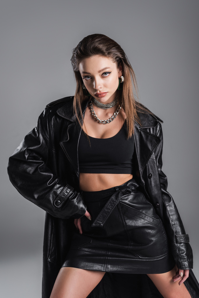 fashionable woman in black leather outfit posing with hand on hip isolated on grey - Foto, Bild