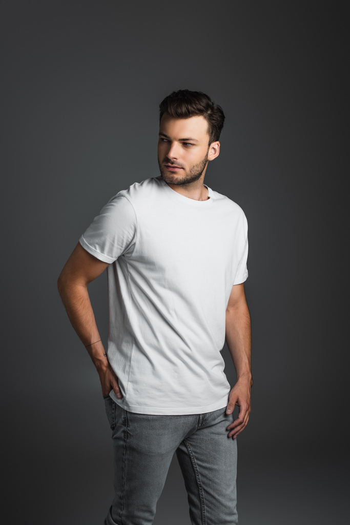 Young man in white t-shirt and jeans looking away isolated on grey  - Fotografie, Obrázek