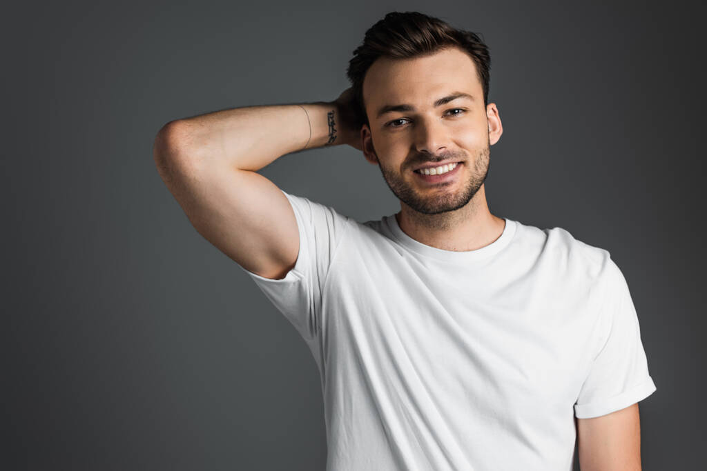 Smiling man in white t-shirt looking at camera isolated on grey  - Foto, Imagem