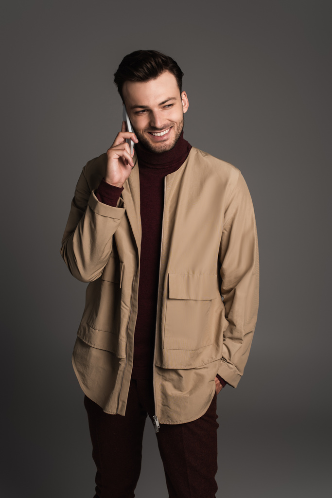 Stylish and smiling man in jacket talking on smartphone isolated on grey  - Photo, image